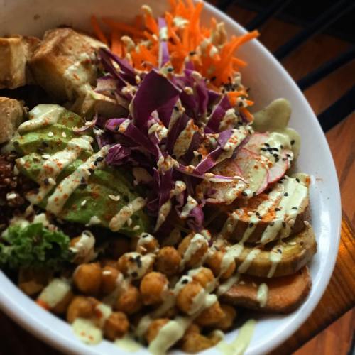 A colorful bowl filled with greens, chickpeas, sliced vegetables, and drizzled sauce, garnished with purple cabbage and carrots.