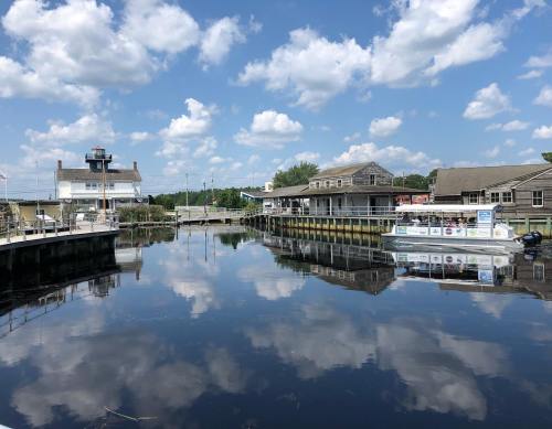 A calm marina with buildings reflecting in the water under a blue sky with fluffy clouds.