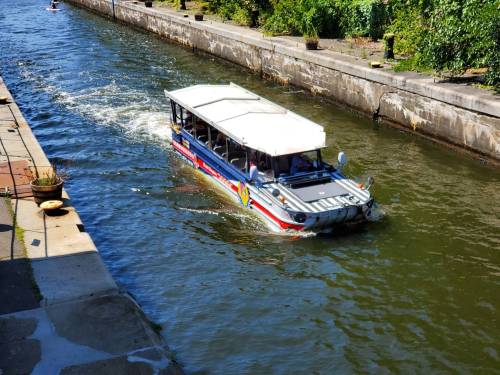 A colorful boat navigates a narrow canal surrounded by greenery and stone walls.
