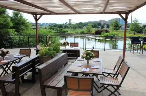 Outdoor dining area with wooden tables and chairs, flowers on tables, overlooking a serene water view.