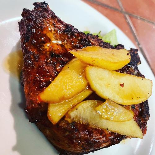Grilled chicken breast topped with caramelized apple slices on a white plate.