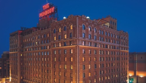 The Peabody Hotel illuminated at night, showcasing its historic brick architecture and iconic rooftop sign.