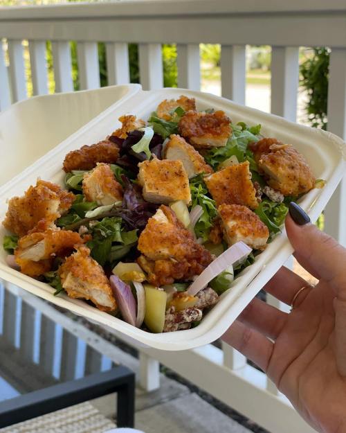 A hand holding a takeout container filled with a salad topped with crispy chicken pieces and mixed greens.