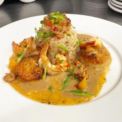 A plate of creamy risotto topped with shrimp, scallops, and colorful garnishes in a rich sauce.