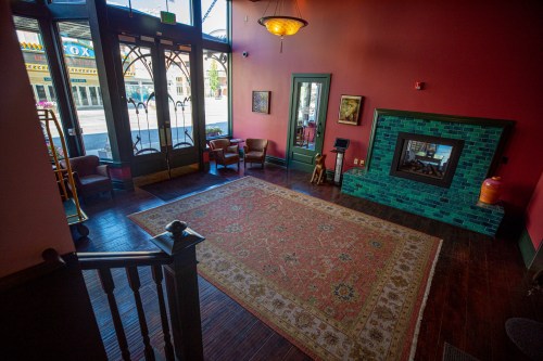 A spacious lobby with a large rug, green fireplace, and seating, featuring large windows and warm red walls.