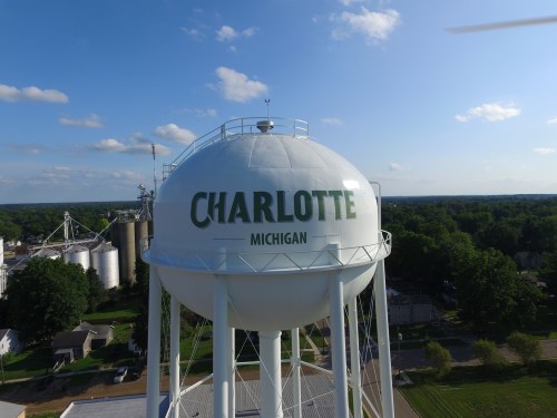 A water tower with "CHARLOTTE" and "MICHIGAN" written on it, surrounded by green trees and a blue sky.