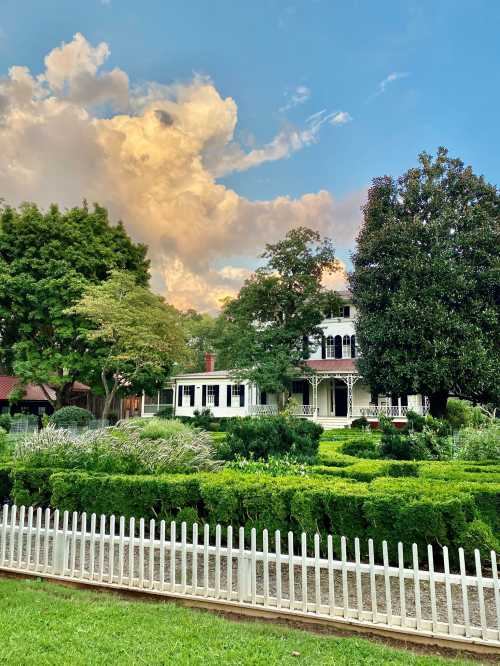 A charming white house surrounded by lush greenery and trees, with a blue sky and fluffy clouds in the background.