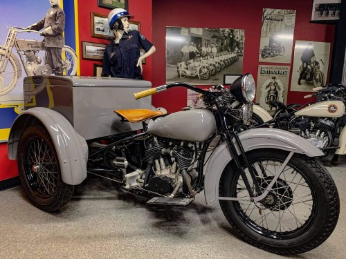 A vintage motorcycle with a sidecar displayed in a museum, surrounded by historical motorcycle photos and memorabilia.