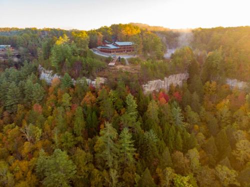 Aerial view of a lodge on a cliff surrounded by vibrant autumn foliage and misty forest.