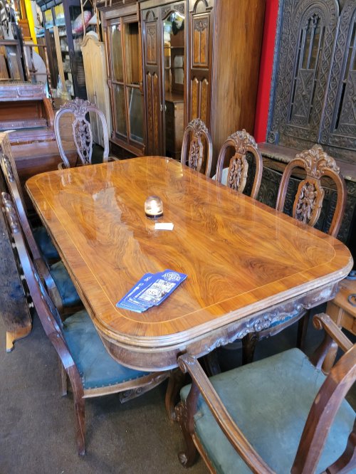 A wooden dining table with intricate carvings, surrounded by ornate chairs, in a vintage furniture store.