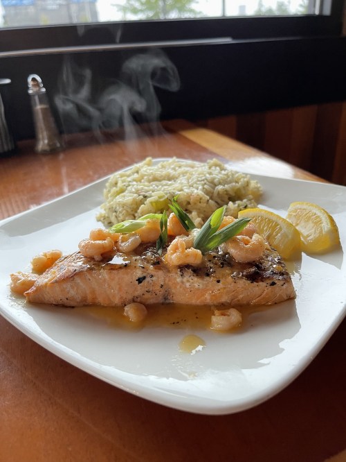 A plate of grilled salmon topped with shrimp and green onions, served with lemon wedges and a side of rice.