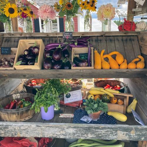 A rustic market display featuring colorful vegetables, herbs, and flowers in wooden crates and baskets.