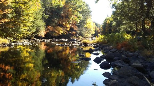 A serene river scene surrounded by colorful autumn foliage and smooth rocks, reflecting the vibrant trees.