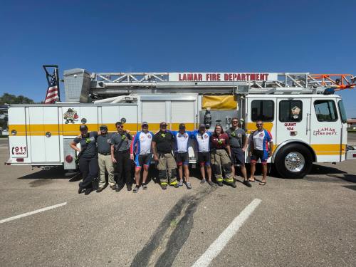 A group of firefighters and community members pose in front of a Lamar Fire Department truck on a sunny day.
