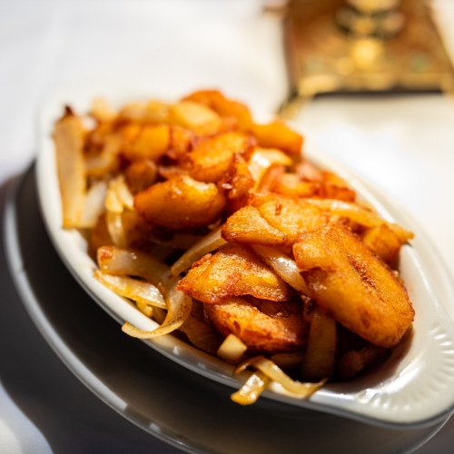 A dish of golden-brown fried potatoes and onions served in a white oval bowl.
