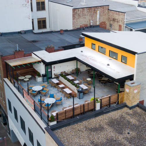 Aerial view of a rooftop restaurant with tables and chairs, surrounded by a cityscape.