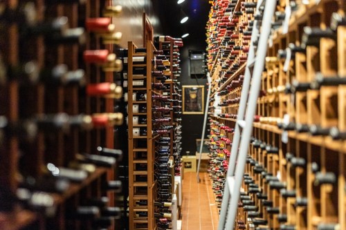 A dimly lit wine cellar lined with wooden racks filled with various bottles of wine.