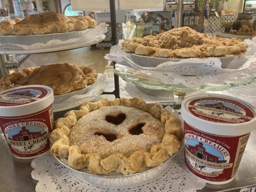 A display of various pies on stands, with two tubs of ice cream in front, all set on a lace doily.