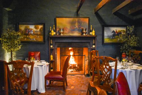 Cozy restaurant interior with a fireplace, elegant dining tables, and paintings of horses on the walls.