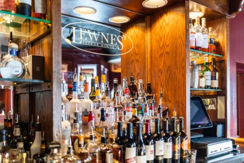 A well-stocked bar at Lewnes' Steak House, featuring various bottles of liquor on wooden shelves.