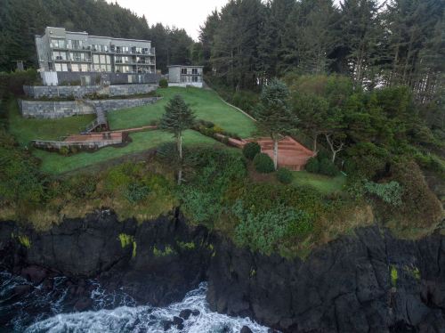 A coastal property with a modern building, lush green lawns, and rocky cliffs overlooking the ocean.