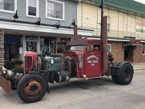 An old fire truck with a red body and large exhaust pipes parked on a street in front of buildings.
