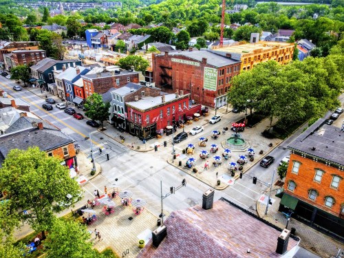 Aerial view of a vibrant street scene with shops, outdoor seating, and greenery in a lively neighborhood.