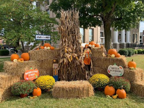 A festive fall display with hay bales, pumpkins, corn stalks, and cheerful signs celebrating the season.