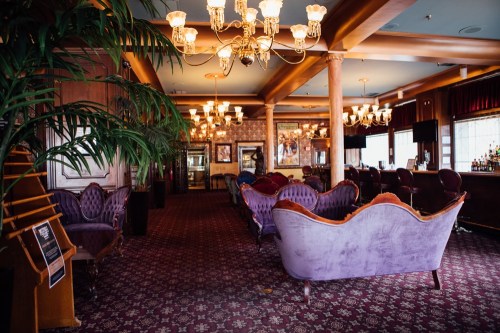 Elegant lounge with plush seating, chandeliers, and a bar, featuring rich colors and a cozy atmosphere.
