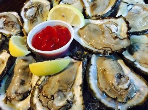 A platter of fresh oysters with lemon wedges and a small cup of cocktail sauce in the center.