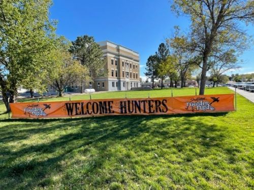A large banner reading "Welcome Hunters" displayed on a grassy area in front of a building and trees.
