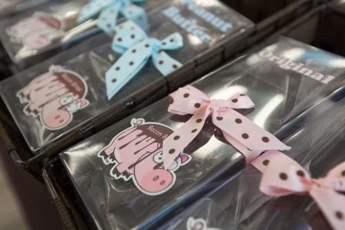 A close-up of packaged treats with colorful ribbons, featuring playful pig graphics and labels like "Peanut Butter" and "Bacon."