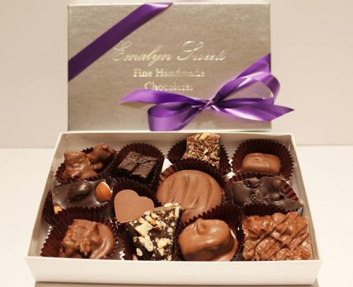 A box of assorted handmade chocolates, elegantly arranged with a purple ribbon on top.