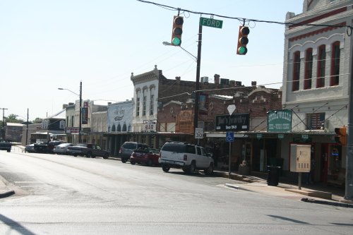 A quiet street scene featuring historic buildings, shops, and parked cars under a traffic light.