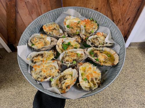 A metal bowl filled with baked oysters topped with cheese and green onions, resting on a textured surface.