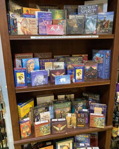 A wooden shelf filled with various tarot and oracle card decks, featuring colorful boxes and titles.
