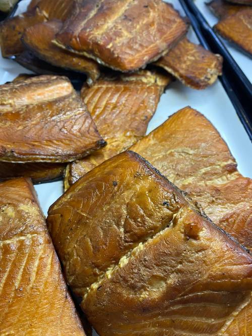 Close-up of smoked fish fillets, showcasing a rich, golden-brown color and flaky texture on a white plate.