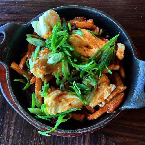 A cast-iron dish filled with crispy fries topped with fluffy scrambled eggs and garnished with green onions.