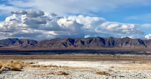 A vast desert landscape with mountains in the background and scattered clouds in a blue sky.