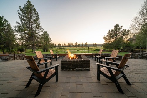 A cozy outdoor seating area with wooden chairs around a fire pit, overlooking a serene landscape at sunset.