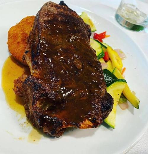 A plate featuring a juicy steak with sauce, a crispy potato cake, and colorful sautéed vegetables.