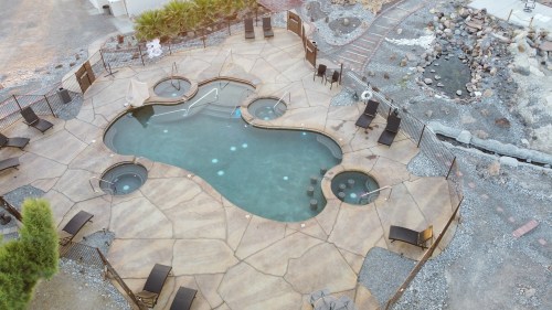 Aerial view of a uniquely shaped pool with spa areas, surrounded by lounge chairs and a rocky landscape.