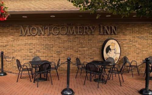 Exterior of Montgomery Inn with a brick wall, outdoor seating, and a decorative sign featuring a chef.