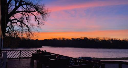 A serene sunset over a river, with vibrant pink and orange hues in the sky and silhouettes of trees along the shore.