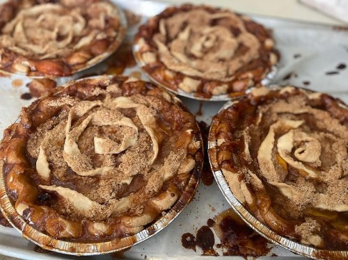 Four apple pies with decorative crusts shaped like roses, sitting on a baking tray with some caramelized filling visible.