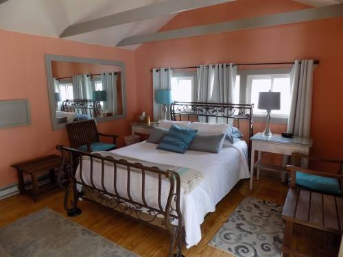 Cozy bedroom with a metal bed frame, light orange walls, wooden furniture, and large windows with curtains.