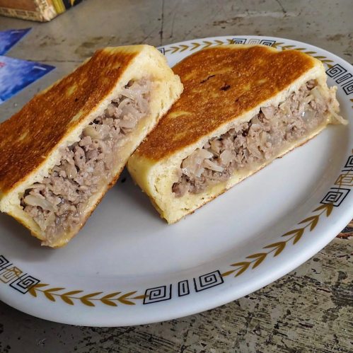 A plate with two halves of a golden-brown stuffed sandwich filled with meat and cabbage.