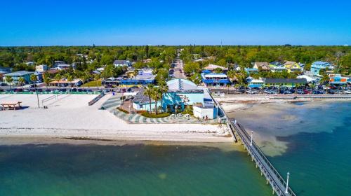 Aerial view of a beachside town with sandy shores, palm trees, and colorful buildings along the waterfront.