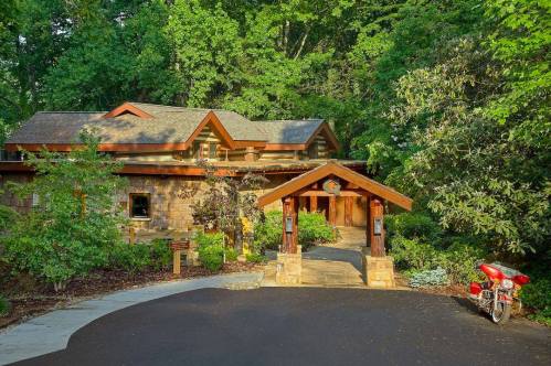 A charming stone house surrounded by greenery, featuring a wooden entrance and a red motorcycle parked nearby.