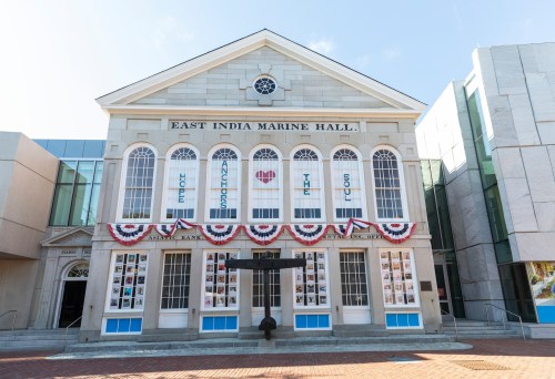 Historic East India Marine Hall with decorative banners and a sculpture in front, set against a clear blue sky.